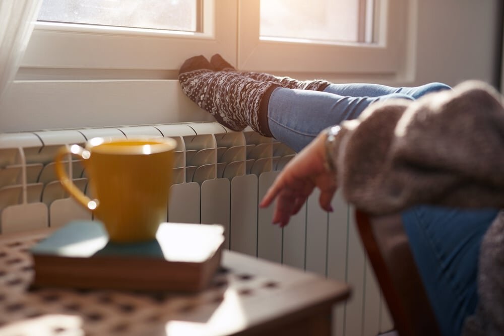 Cosy interior scene showing a person with their feet on a radiator, enjoying the warmth. Proper insulation from EWI Store helps maintain a consistent indoor temperature, keeping homes comfortable and energy-efficient throughout winter.