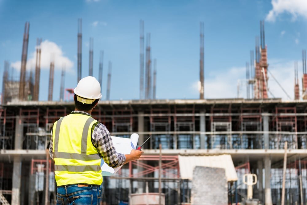Construction site with a foreman in a high-visibility vest reviewing blueprints in front of a reinforced concrete building under development. EWI Store provides essential render and insulation solutions tailored for large-scale commercial projects.