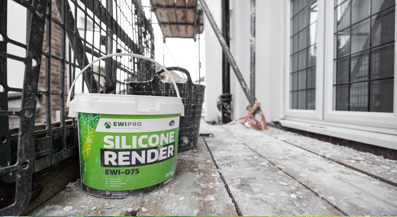 On-site photo of EWI Pro Silicone Render (EWI-075) in a 25kg bucket, positioned beside scaffolding. This ready-to-use, hydrophobic render is ideal for external insulation systems, offering UV resistance, durability, and premium aesthetic—available now from EWI Store.