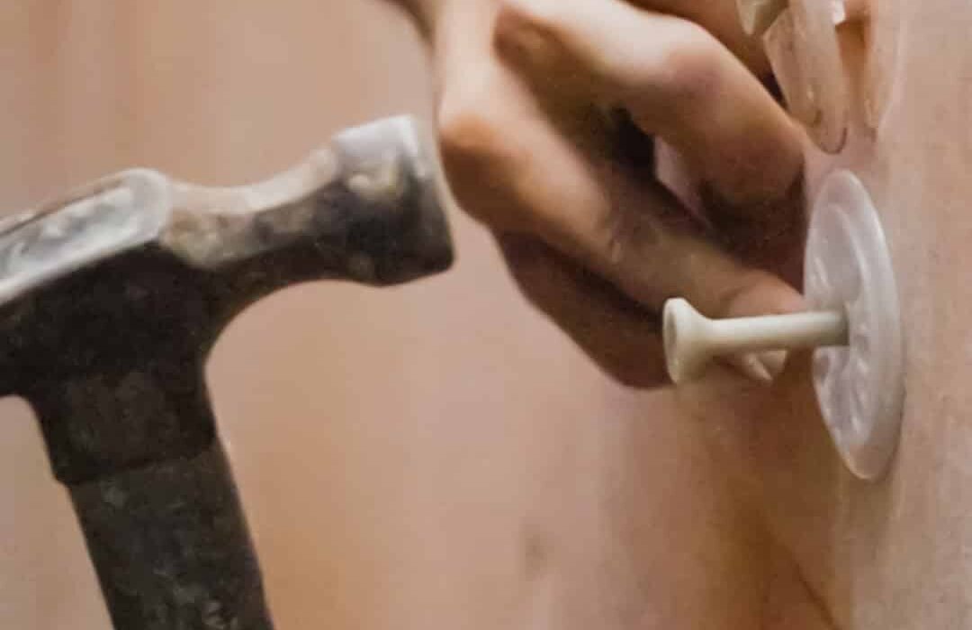 Close-up of mechanical fixings being hammered into insulation boards. These washers secure EPS or mineral wool boards to the substrate before basecoat application. EWI Store offers a full range of fixings designed for stability and long-term performance in EWI systems.