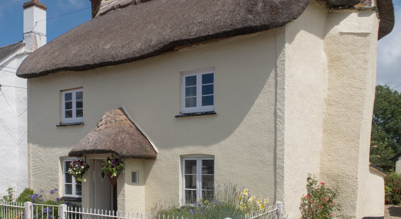 Thatched cottage with a pale cream-coloured render finish on the exterior walls. The breathable render helps regulate moisture in heritage properties while preserving traditional aesthetics. EWI Store supplies lime and silicone-based renders for period homes.