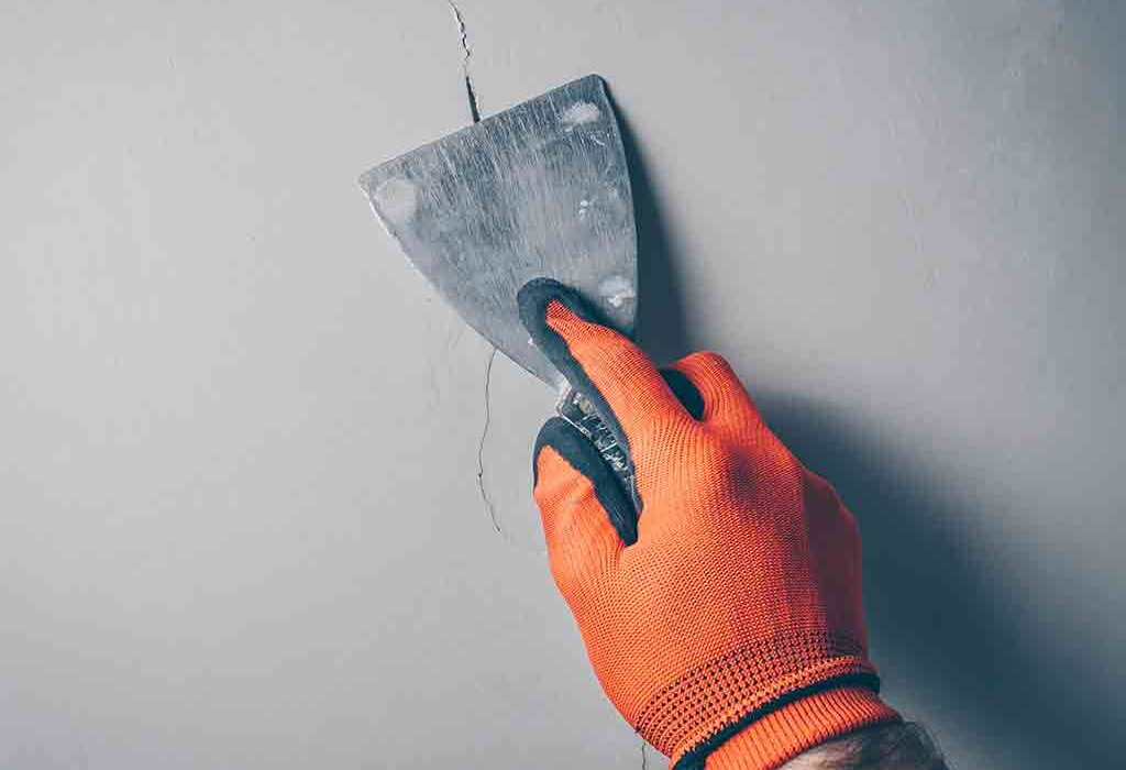 Close-up of a cracked internal wall being scraped and prepared for repair. Proper surface preparation is essential before applying fillers, basecoats, or finishing layers. EWI Store offers a wide selection of internal repair and preparation products for plaster and paint systems.