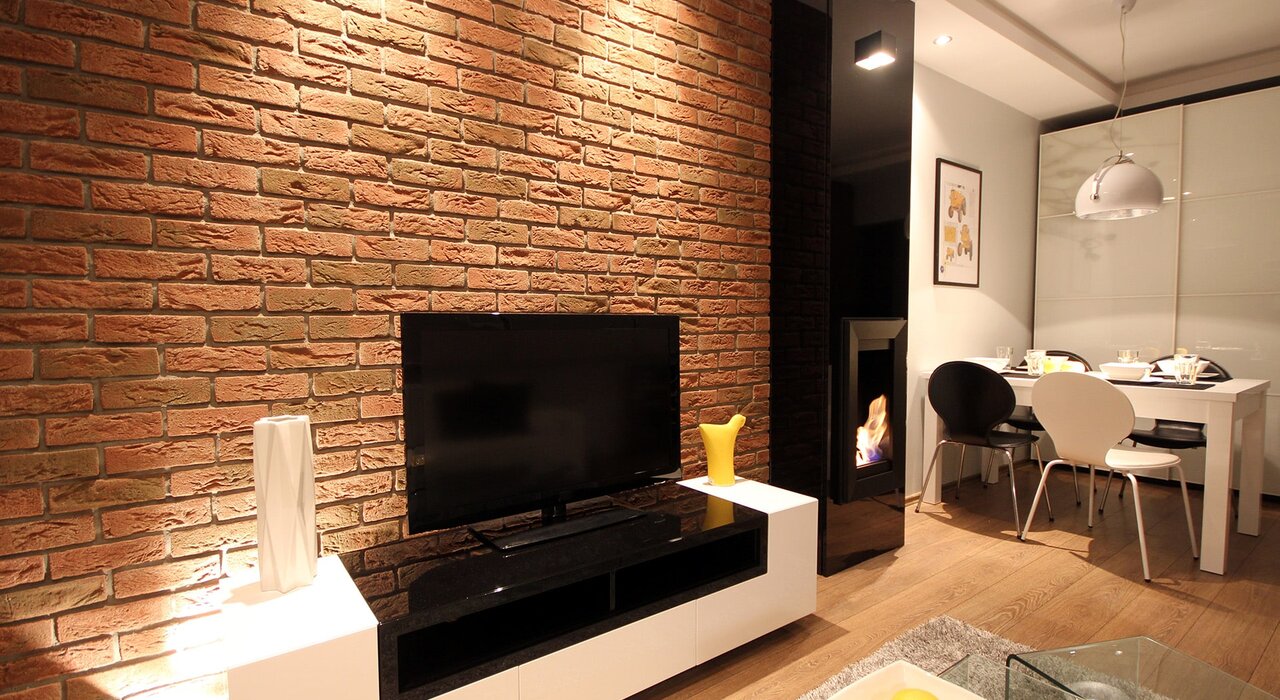 Modern interior space featuring a brick-effect accent wall behind a flat-screen TV. This decorative brick finish adds character while complementing modern furniture. EWI Store offers similar effect renders and cladding systems for creating a rustic, exposed brick appearance.