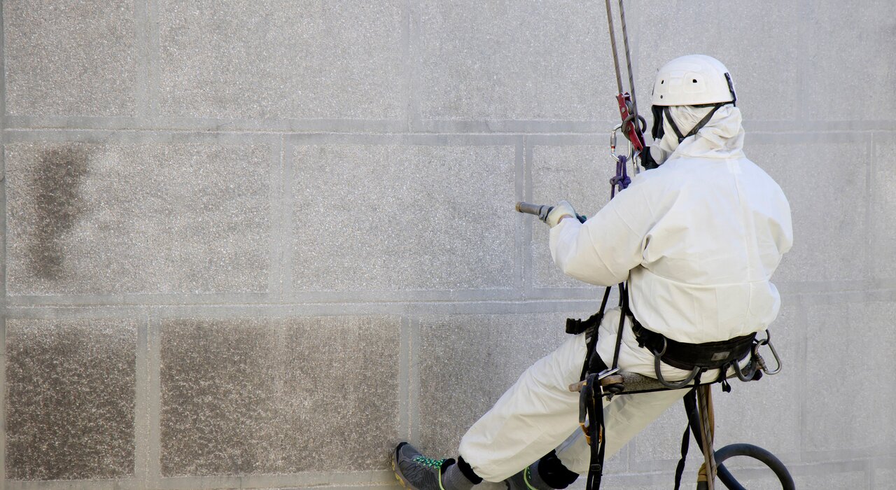 Technician carrying out façade cleaning or coating removal using industrial rope access. This method allows safe and effective maintenance or preparation work on high-rise or difficult-to-reach walls. EWI Store offers a range of façade cleaners and breathable coatings ideal for refurbishment projects.