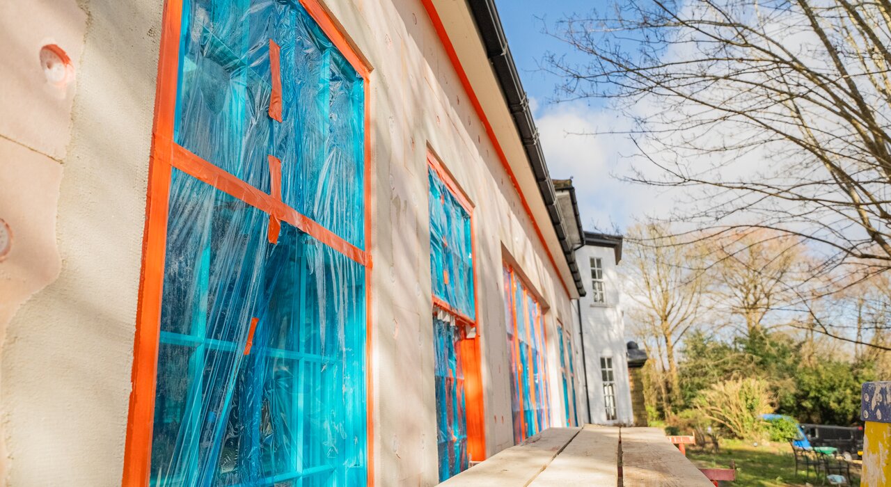 Installation of EPS insulation boards on a detached property, with windows protected using red masking tape and blue film. EPS boards, available from EWI Store, provide excellent thermal performance and are a cost-effective solution for upgrading external walls as part of a full EWI system.