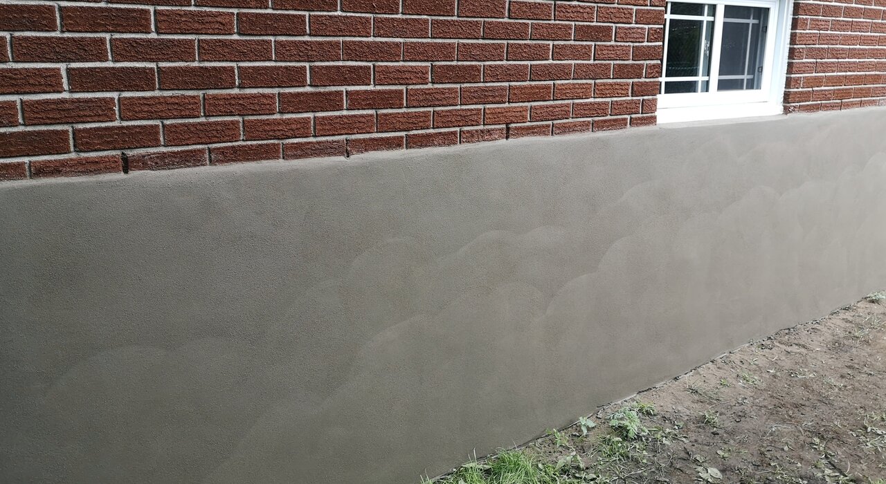 Newly rendered plinth area beneath a brick façade, finished with a smooth, uniform coat. EWI Store supplies durable basecoat and render systems specifically designed for plinths, providing enhanced resistance to moisture, impact, and dirt in high-exposure zones.