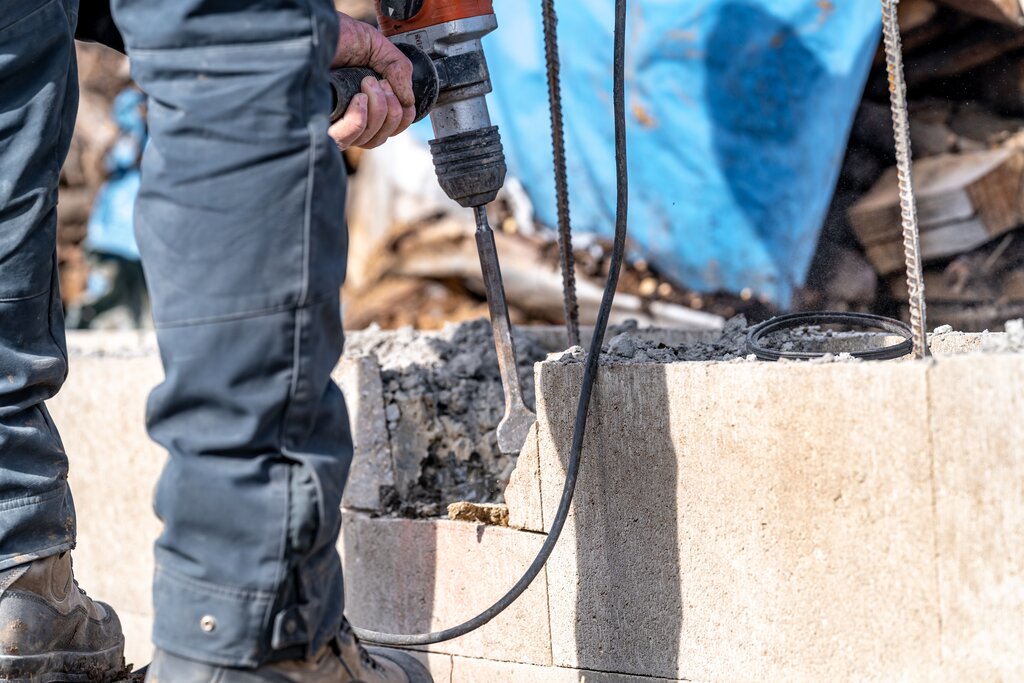Close-up of a worker using a demolition hammer to break apart a damaged concrete wall. For structural repairs or render replacement, EWI Store supplies the full range of EWI Pro basecoats, adhesives and reinforcements for reliable substrate preparation.