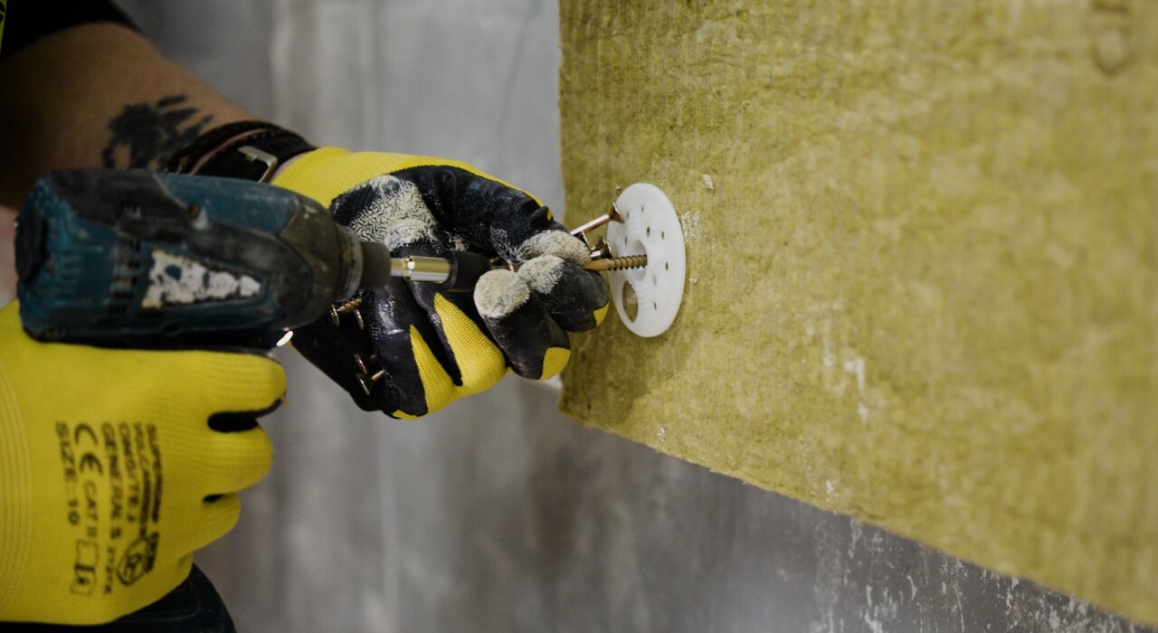 Close-up of a worker using a power drill to install insulation fixings through mineral wool boards. Available at EWI Store, these fixings ensure secure attachment of insulation panels, providing long-term thermal efficiency and stability in external wall insulation systems.