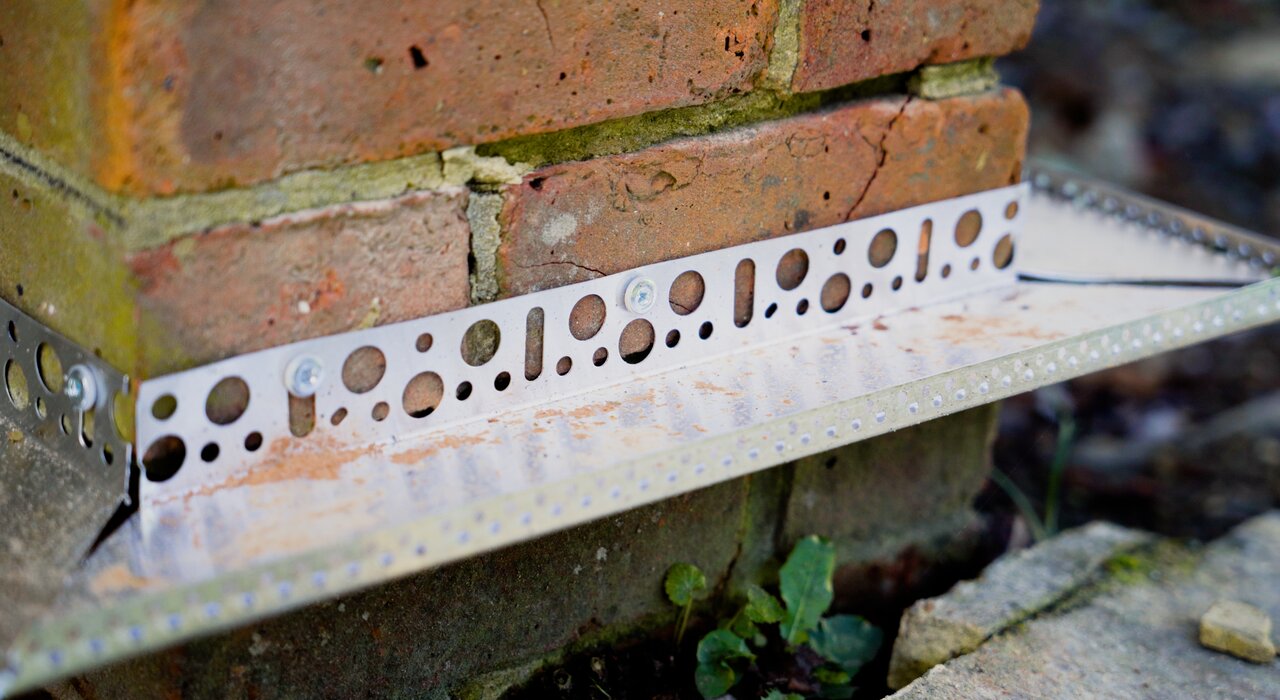 Close-up of a stainless steel EWI Pro starter track installed at the base of a brick wall. Starter tracks provide a secure and level foundation for external wall insulation systems, helping to prevent moisture ingress and ensure clean, straight lines. Available from EWI Store, our range of profiles and accessories ensures a professional and long-lasting EWI installation.