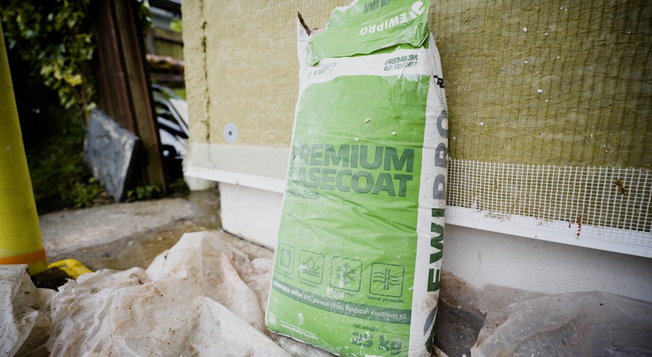 Bag of EWI Pro Premium Basecoat resting against a wall with visible mesh and insulation. This high-performance basecoat is formulated for superior adhesion and crack resistance, forming a strong foundation for render finishes. Available at EWI Store, it’s ideal for use with both EPS and mineral wool insulation systems.