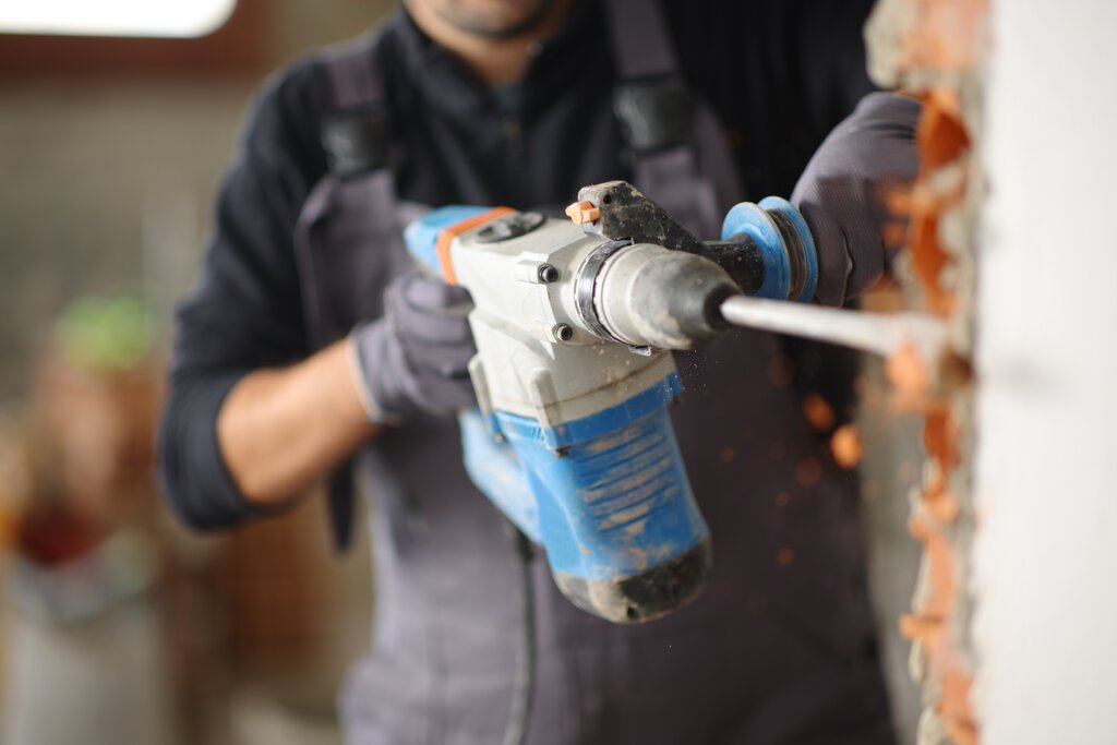 Close-up of a worker using a powerful rotary hammer drill to break through a brick wall. Ideal for renovation and installation work, this tool ensures fast and efficient penetration in masonry, helping prepare walls for external wall insulation systems.