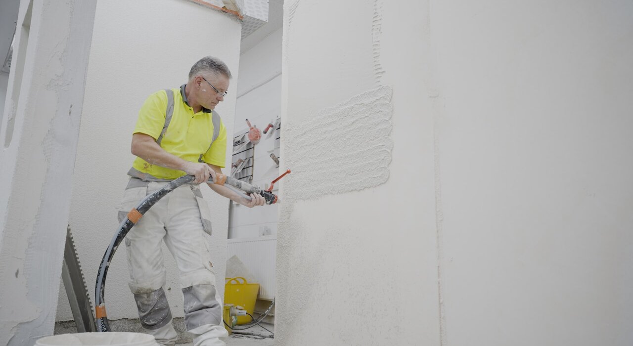 Interior application of plaster using a spray machine. Machine-applied basecoats offer a consistent and time-saving solution for internal wall finishes, enhancing adhesion and surface uniformity before applying topcoat render or decorative finishes.