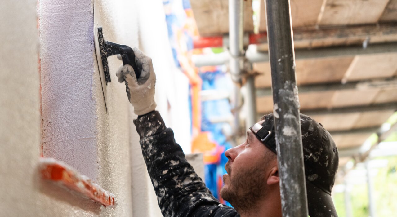 Professional applicator smoothing topcoat render on an external wall using a plastic float. Available from EWI Store, our range of silicone and mineral renders ensures a durable, breathable, and weather-resistant finish in any façade insulation system.