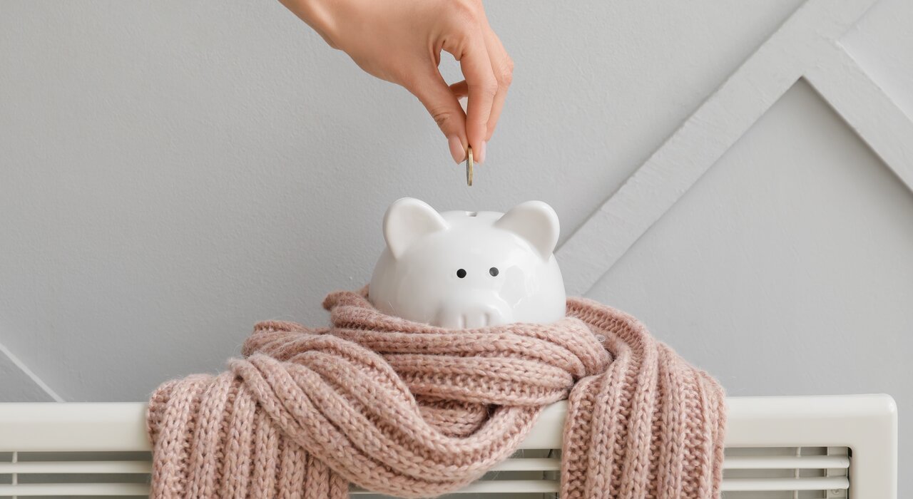 Piggy bank wrapped in a scarf on top of a radiator, symbolising energy savings. Investing in EWI Store insulation systems significantly reduces heating costs and improves indoor comfort year-round. A smart choice for sustainable savings.