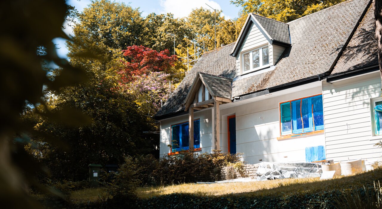 Detached house undergoing external wall insulation works, with windows protected by blue sheeting. EWI Store supplies all necessary materials for professional-grade EWI installations, from basecoats to topcoat renders, ensuring a weather-resistant and energy-efficient finish.