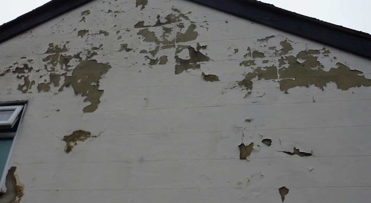 Close-up of a rendered gable wall with extensive cracking and flaking paint. EWI Store recommends proper insulation and breathable renders to prevent damp-related damage and preserve the longevity of building facades.