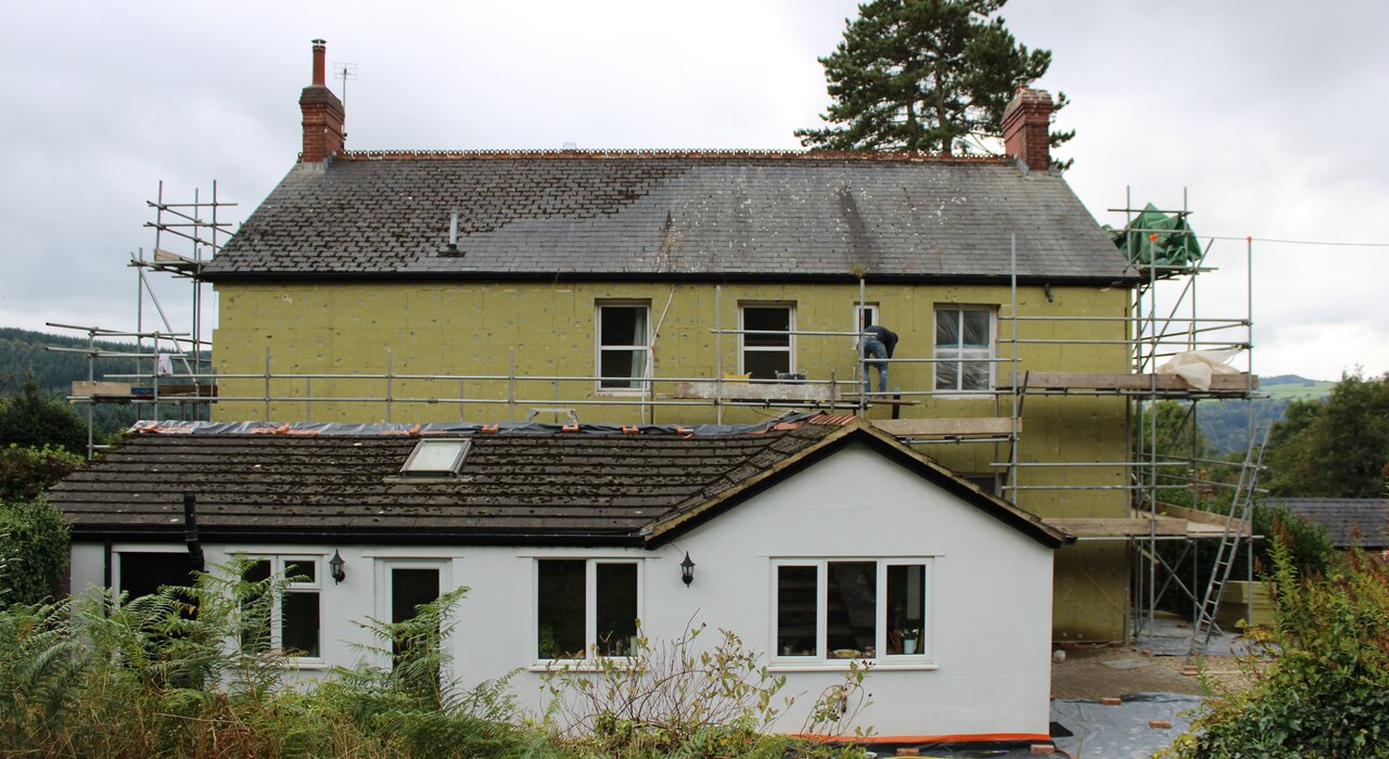 External wall insulation being installed on a detached property with scaffolding in place. High-performance mineral wool boards from EWI Store deliver superior fire resistance, soundproofing, and thermal efficiency.